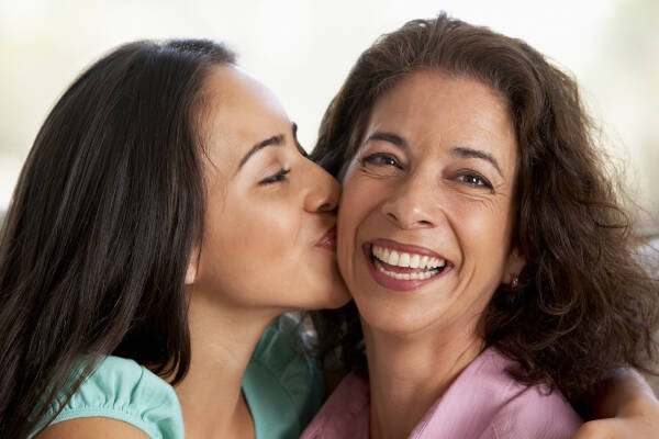 A close-up shot captures the moment when a daughter plants a gentle kiss on her 50-year-old mother's cheek at home.