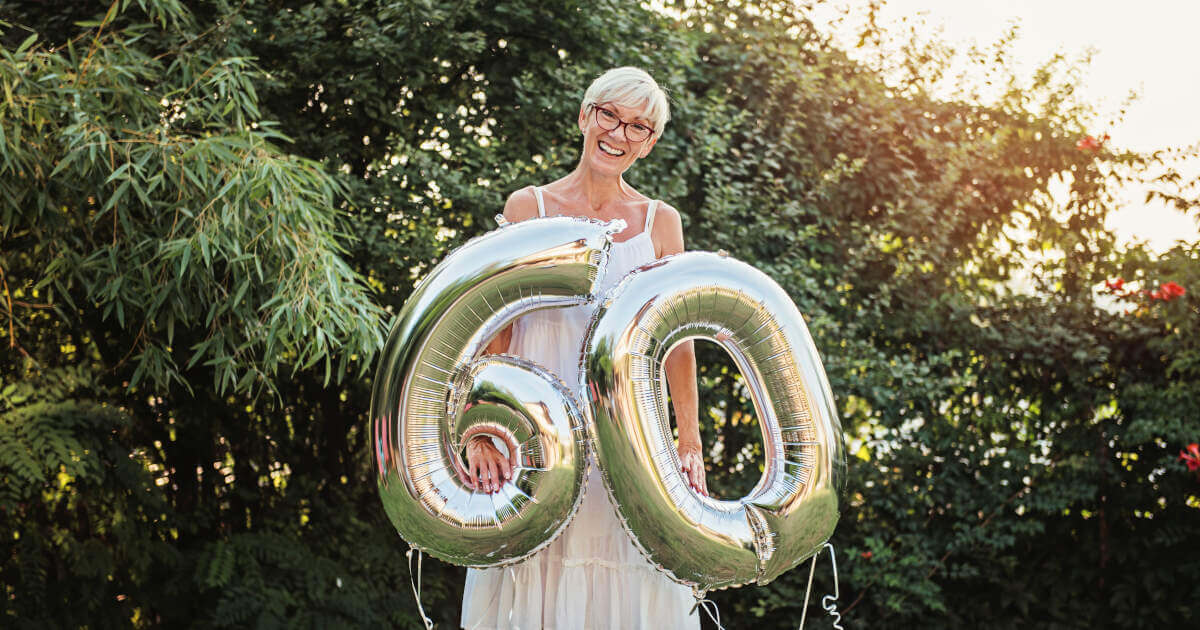 Senior woman celebrating her 60th birthday, holding 60th birthday balloons.