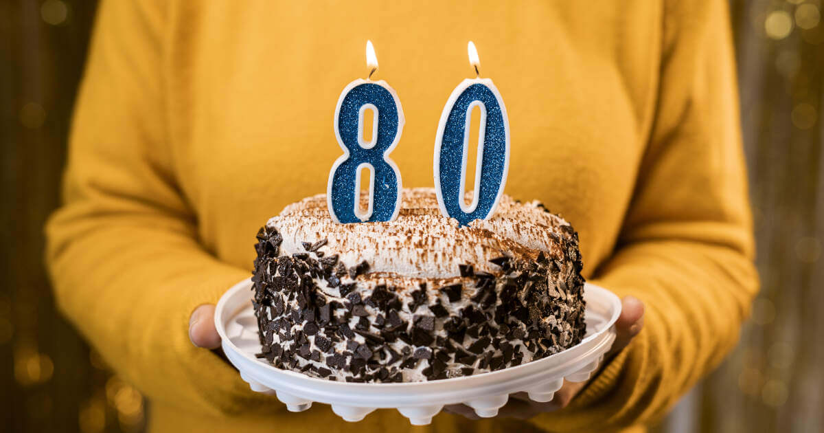 Close-up view of a woman celebrating her 80th birthday with a delightful festive cake adorned with number 80 candles.
