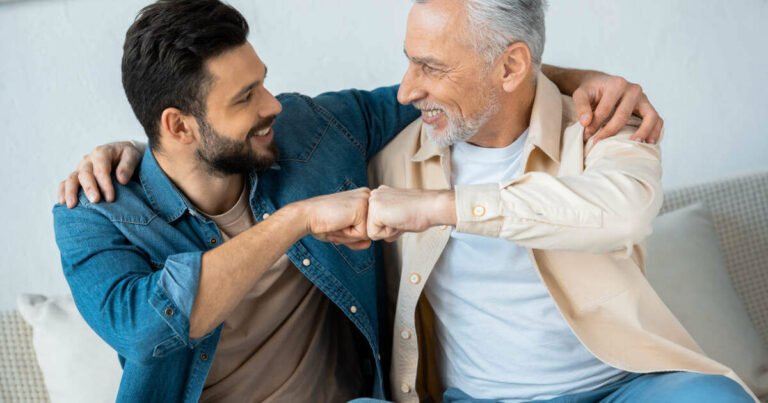 Cheerful retired father fist-bumping with happy bearded son at home - heartwarming Father's Day wishes for son.