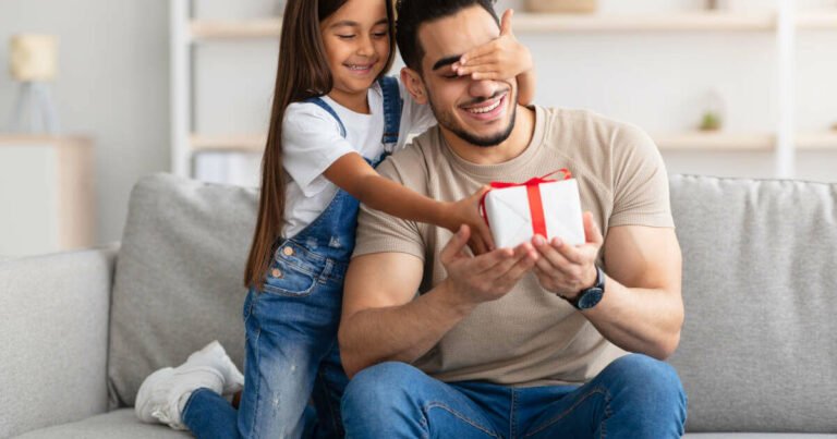 Excited dad with eyes covered, receiving a heartwarming surprise from his cute little girl at home.