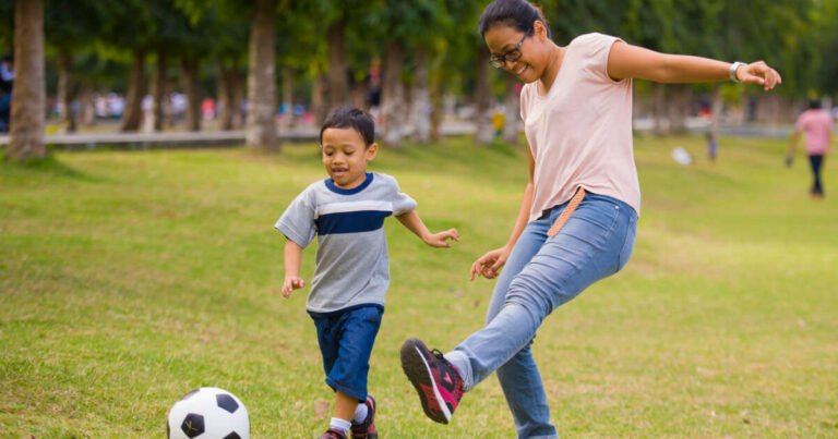 Mother playing football with her son in the park. Both are having great fun.