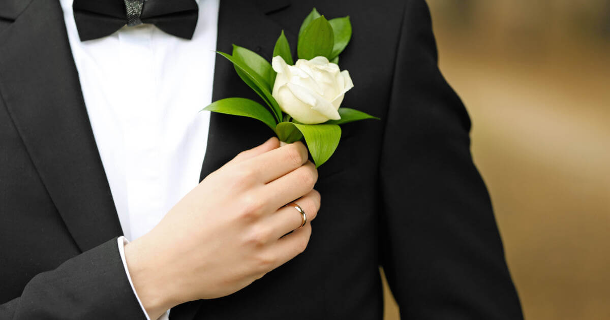 Groom dressed in a suit, looking dashing as he holds a buttonhole, anticipating the beautiful moments ahead.