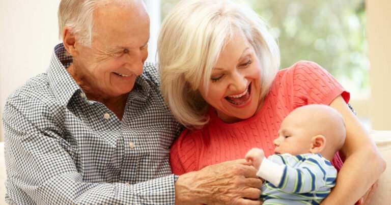 Senior couple sitting on sofa embracing their precious baby grandson, cherishing the special bond they share.