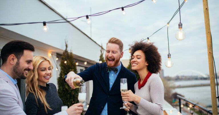 Two couples celebrating an anniversary on an outdoor terrace, pouring champagne to toast the occasion.