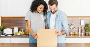 Happy couple, standing in their modern kitchen, eagerly opening a gift with excitement.