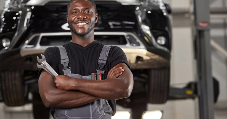 Cheerful auto mechanic in uniform posing at work, holding two spanners in his hand.