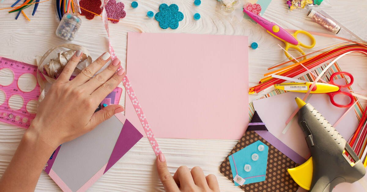 Woman's hand delicately cutting paper, in the act of scrapbooking.