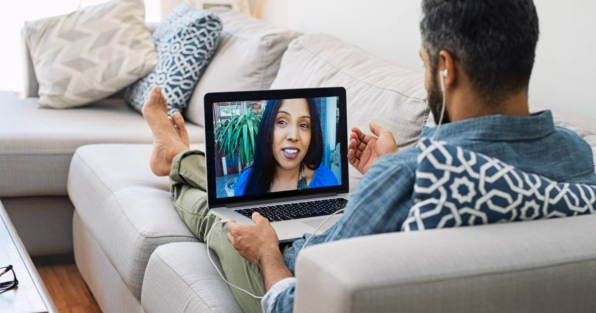 Rear view of a husband relaxing on the couch, sharing heartfelt moments with his wife through a video chat on the laptop.
