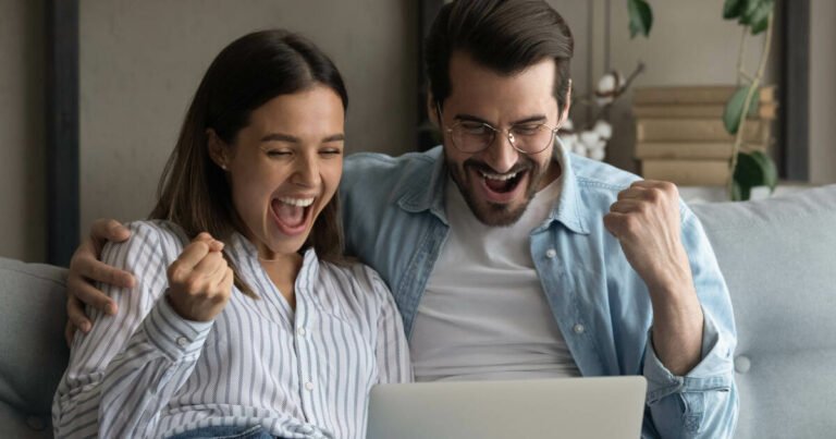 Joyful young couple celebrating husband's new job, looking at computer.