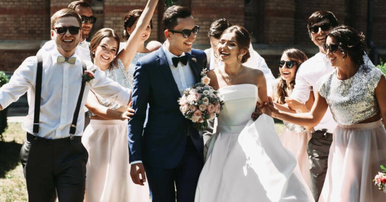 Newlywed couple, surrounded by their joyful bridesmaids and groomsmen, having fun and celebrating outdoors.