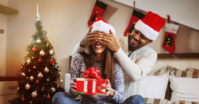 A man covering his girlfriend's eyes while presenting her with a gift.