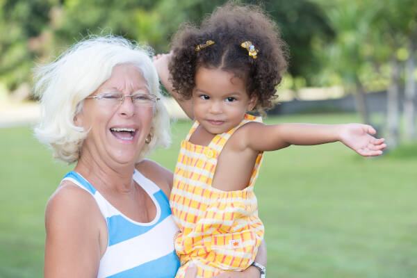 1 year old girl holds her arms out as her grandmother holds her and smiles at the local park.