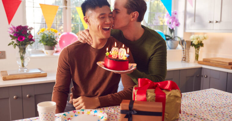 Same-sex male couple celebrating a 30th birthday at home with a cake and presents.
