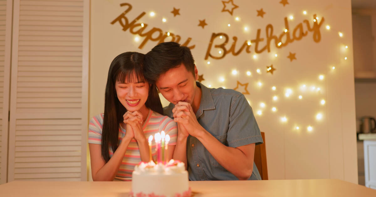 An Asian couple celebrating a birthday at home and making wishes.