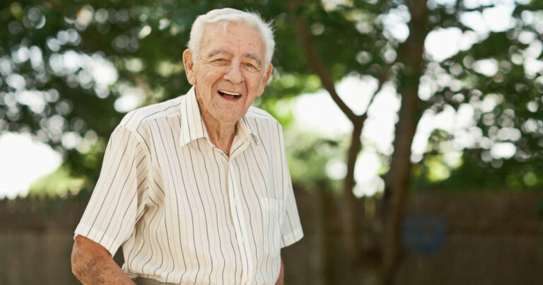 Laughing 90-year-old senior man stands outside in his backyard