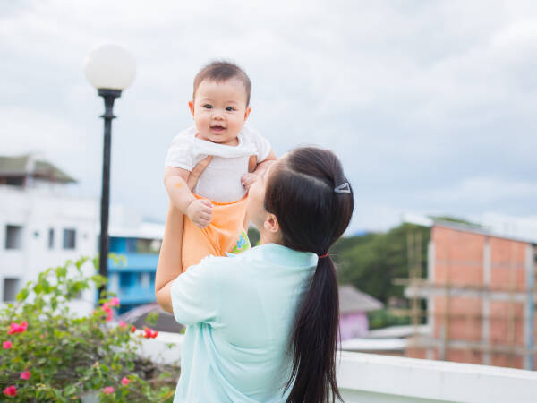 A baby girl is being held up in the air by her aunt as they stand outside.