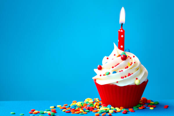 A birthday cupcake with colorful sprinkles and a single candle against a light blue background.