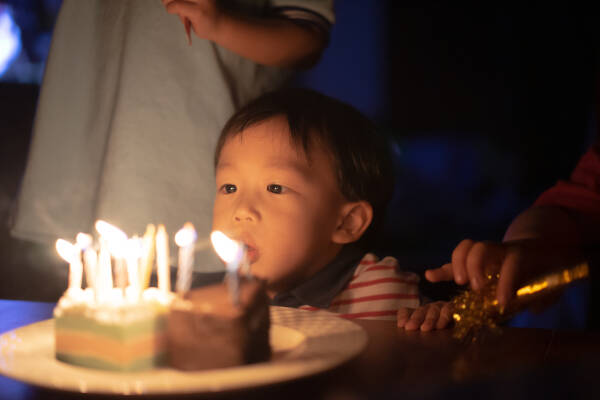 A happy kid blows out candles on his birthday cake during a night time birthday party.