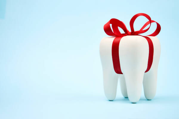 A tooth wrapped up with a red gift bow against a light blue backdrop