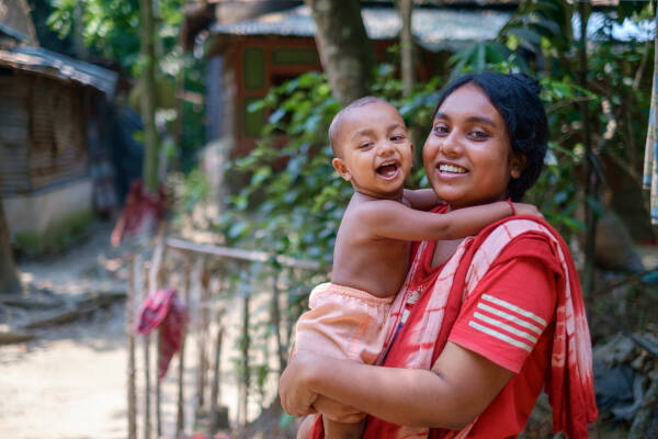 A young teenage auntie stands outside, holding her baby nephew in her arms, both smiling happily