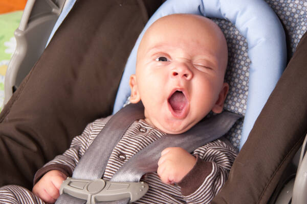 Adorable baby boy yawns humorously while seated in safety seat