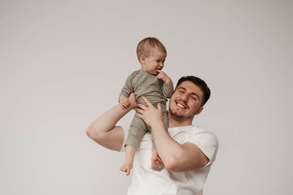 An uncle holds his niece on his shoulders as they both smile against a grey backdrop.