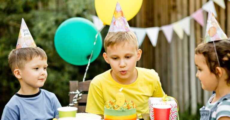 A cute and funny nine-year-old boy celebrates his birthday with family or friends, blowing out candles on a homemade cake in the backyard.