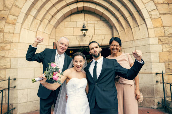 Bride and groom cheer as two of their parents stand behind them, everyone happy on their wedding day