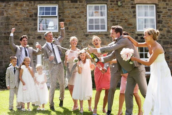 Bride and groom opening champagne in front of parents and family, everyone smiling