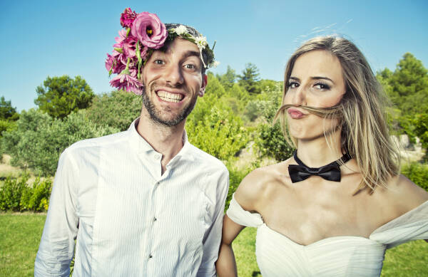 Bride and groom posing for photo; groom pulls a funny face while the bride uses her hair to create a mustache