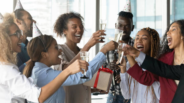Businesspeople raise a toast to their boss, who holds a present; everyone smiles and is happy
