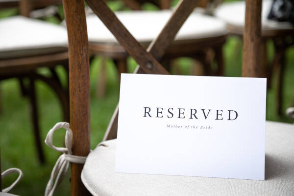 Close-up 'Reserved Mother of the Bride' sign on seat cushion at outdoor wedding