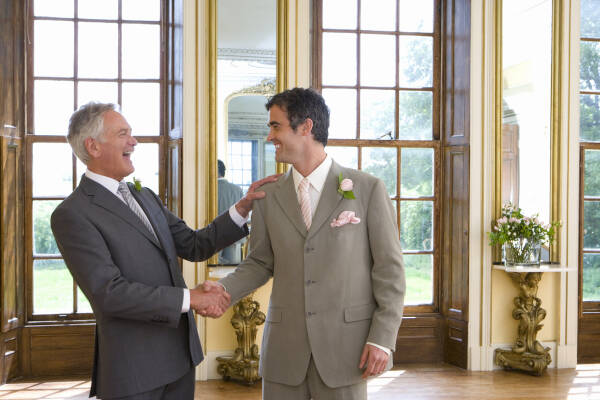 Dad laughs as he shakes his son's hand on son's wedding day