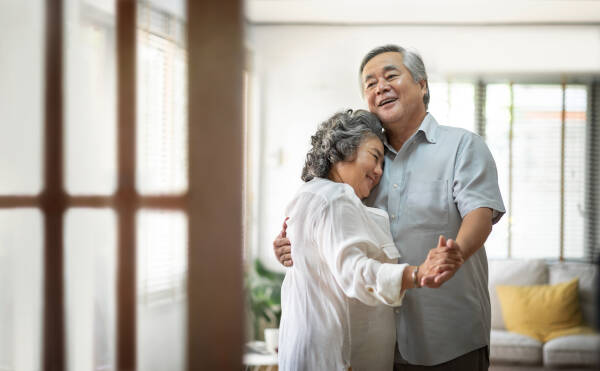 Elderly couple dancing and smiling in their living room at home