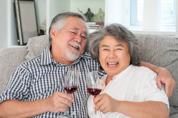 Elderly couple smiles while holding a wine glass on sofa at home