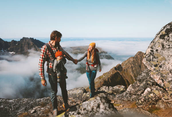 Family hiking in mountains, man and woman with baby carrier, enjoying outdoor lifestyle.