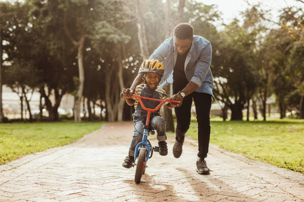 Father teaching his son how to ride a bike in the park, both smiling