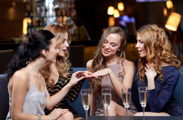 Four women sit around a table admiring one of the women's newly acquired engagement rings