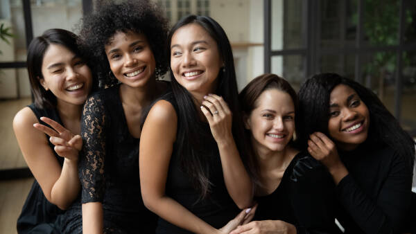 Happy bride showing off her engagement ring with four bridesmaids wearing elegant black dresses, all looking at the camera.