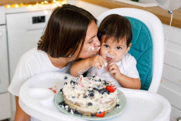 Happy mother celebrates first birthday with one-year-old baby in a white kitchen