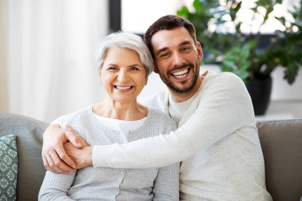 Happy, smiling senior mother embraces her adult son warmly at home.