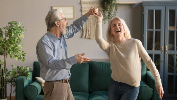 Joyful retired romantic couple dances and laughs in the living room