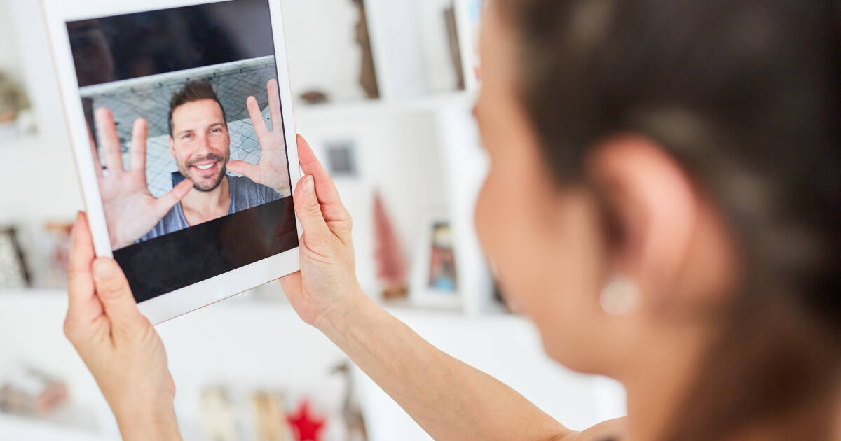 A young woman using a tablet computer to video chat with her partner online.