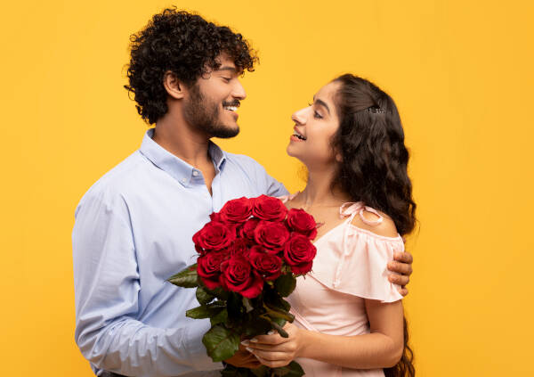 Loving couple embraces, holding a bouquet of flowers, gazing at each other against a yellow background.