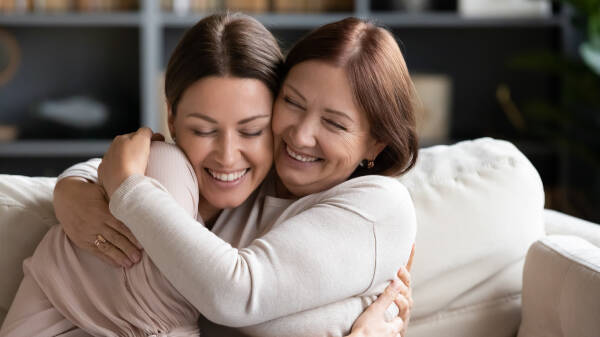 Loving middle-aged mother cuddling her daughter-in-law as they share smiles and laughter.