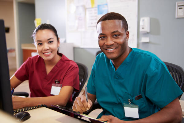 Male and female nurses collaborate at the nurses' station, sharing smiles as they work together