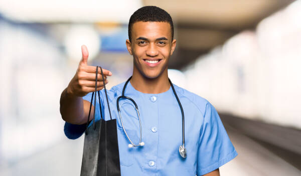 Male nurse smiles while holding out a shopping bag in a hospital