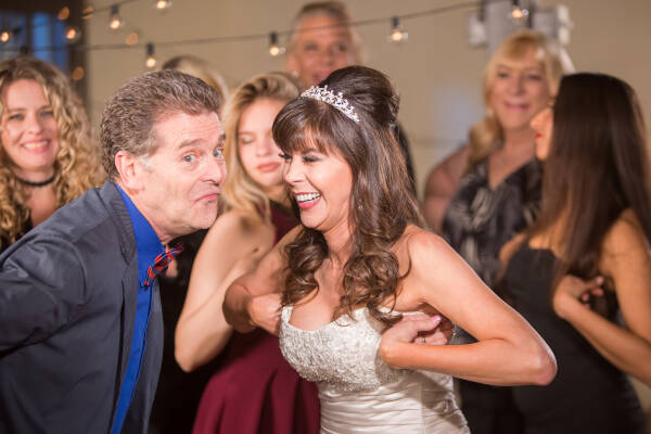 Man and bride doing the chicken dance at a wedding, with family in the background