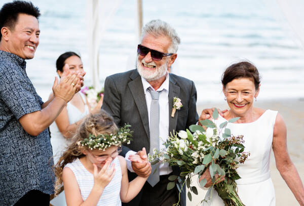 Mature couple getting married on the beach while their adult son claps in the background